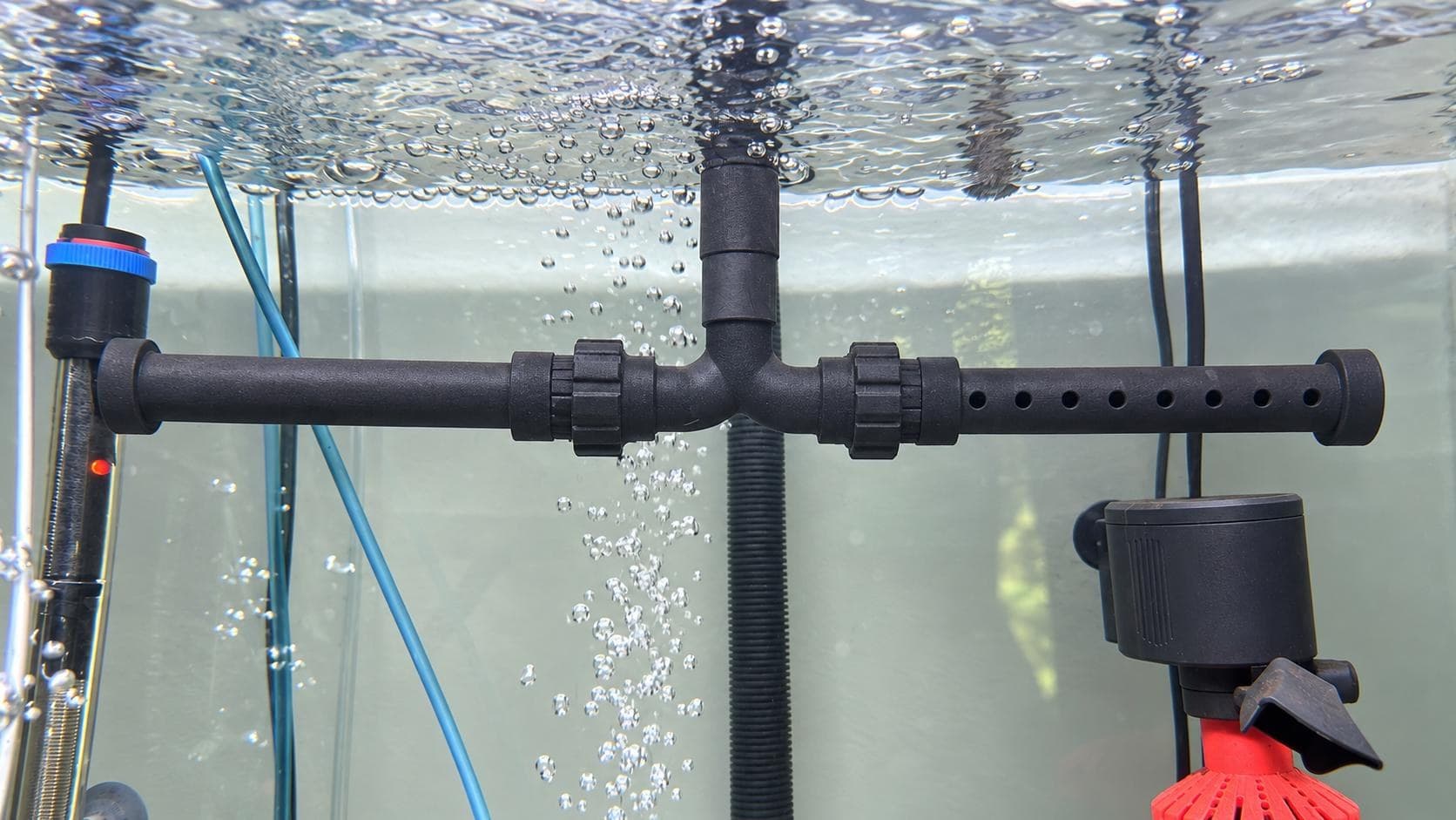 Spray bar installed along the back of a working aquarium, with bubbles rising past the inlet